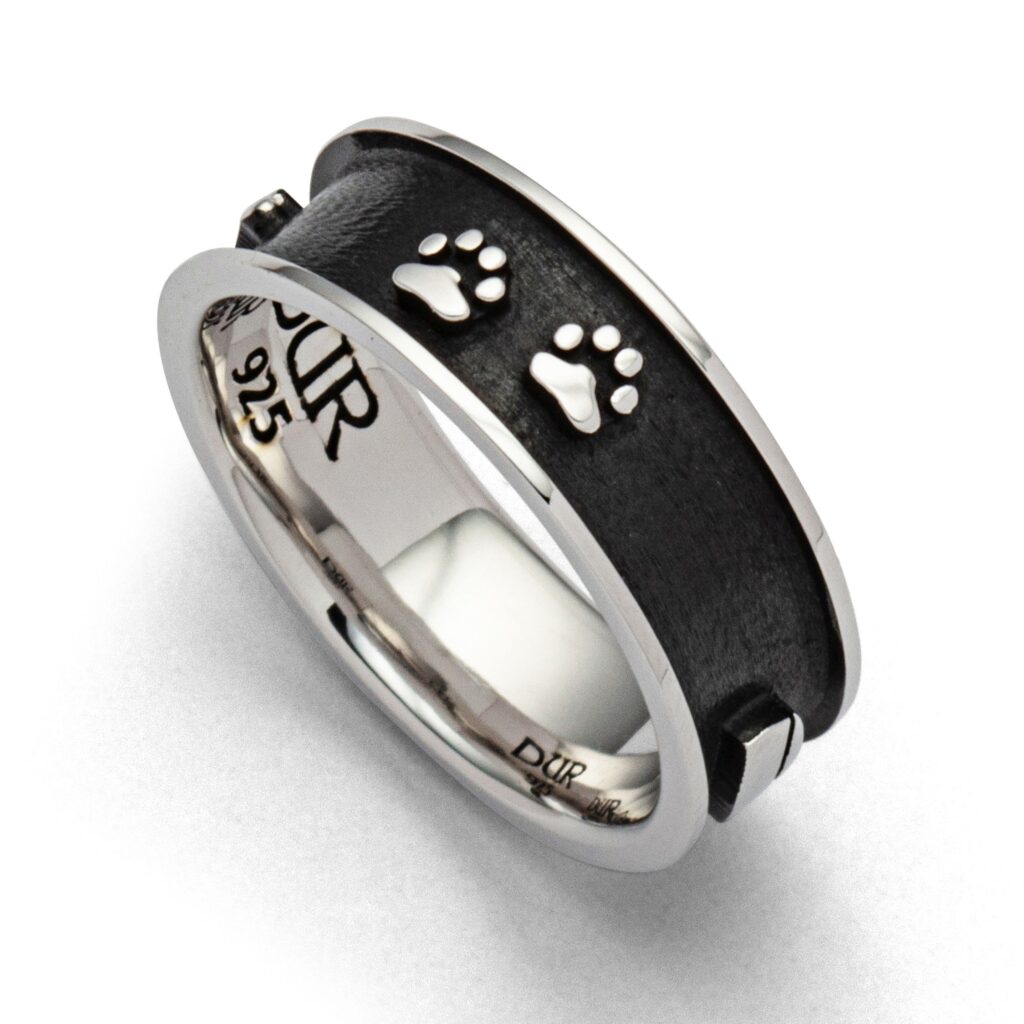 Ring „Lucky Dog 2.0“ (R5621) aus 925er Sterling-Silber, schmaler Bandring mit liebevoll gestalteten Motiven rund um das Thema Hund. Die Kombination aus glänzenden Elementen und dunklem Hintergrund verleiht dem Ring eine moderne, kontrastreiche Optik. Fein ausgearbeitete Details wie Hundepfoten, Napf und Knochen machen den Ring zu einem ausdrucksstarken Begleiter für Hundeliebhaber. Die Motive heben sich plastisch von der dunkel rhodinierten Innenfläche ab und rücken die emotionale Verbindung zum Vierbeiner stilvoll in den Fokus. Außen hell rhodiniert und innen dunkel gehalten entsteht ein spannendes Zusammenspiel aus Licht und Tiefe. Die Rhodinierung verleiht dem Ring einen besonders langlebigen Glanz und schützt das Silber zusätzlich vor dem Anlaufen. Ein dezentes, aber bedeutungsvolles Schmuckstück für den Alltag.